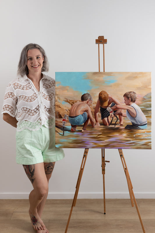 Woman standing next to a painting of children by a river on an easel.